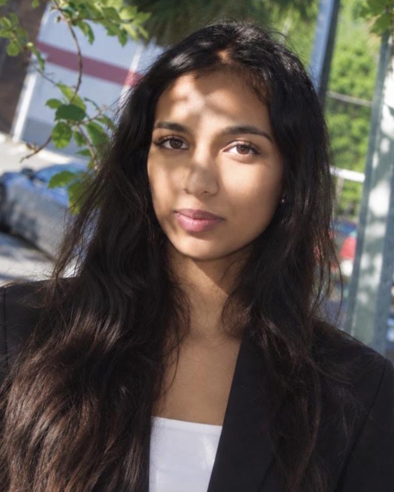 Soni Reddy in a black blazer, standing outside in dappled sunlight